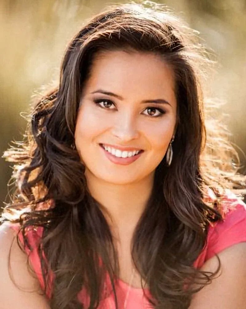 Idaho high school senior with long dark hair smiling in a pink top, photographed outdoors in soft natural light.