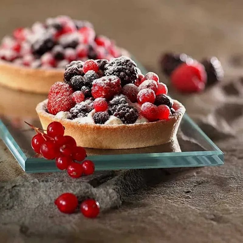 Close-up of two fruit tarts filled with fresh raspberries, blackberries, red currants, and powdered sugar, placed on a glass tray over a textured surface—captured by Idaho Photography Studios.