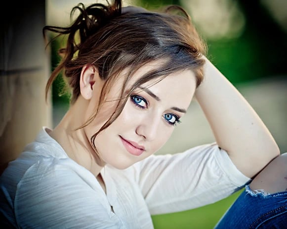 Timberline High senior in white top and jeans, leaning with arm on head, surrounded by soft greenery and natural light