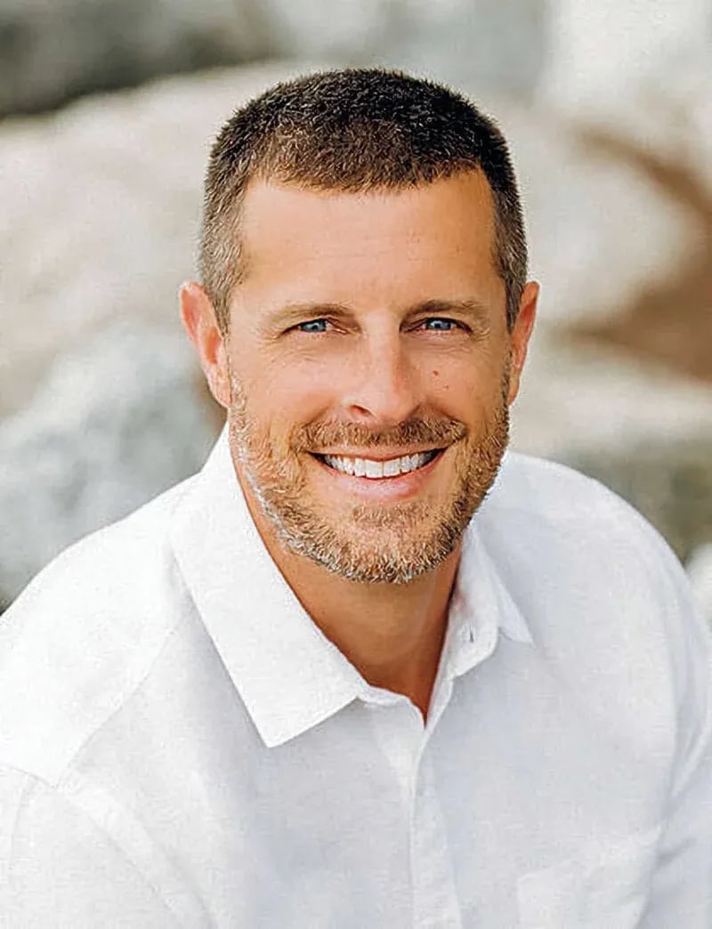 Casual business headshot of a smiling man with short brown hair and trimmed beard, wearing a white button-up shirt in an outdoor setting with light-colored rocks—photographed by Idaho Photography Studios.