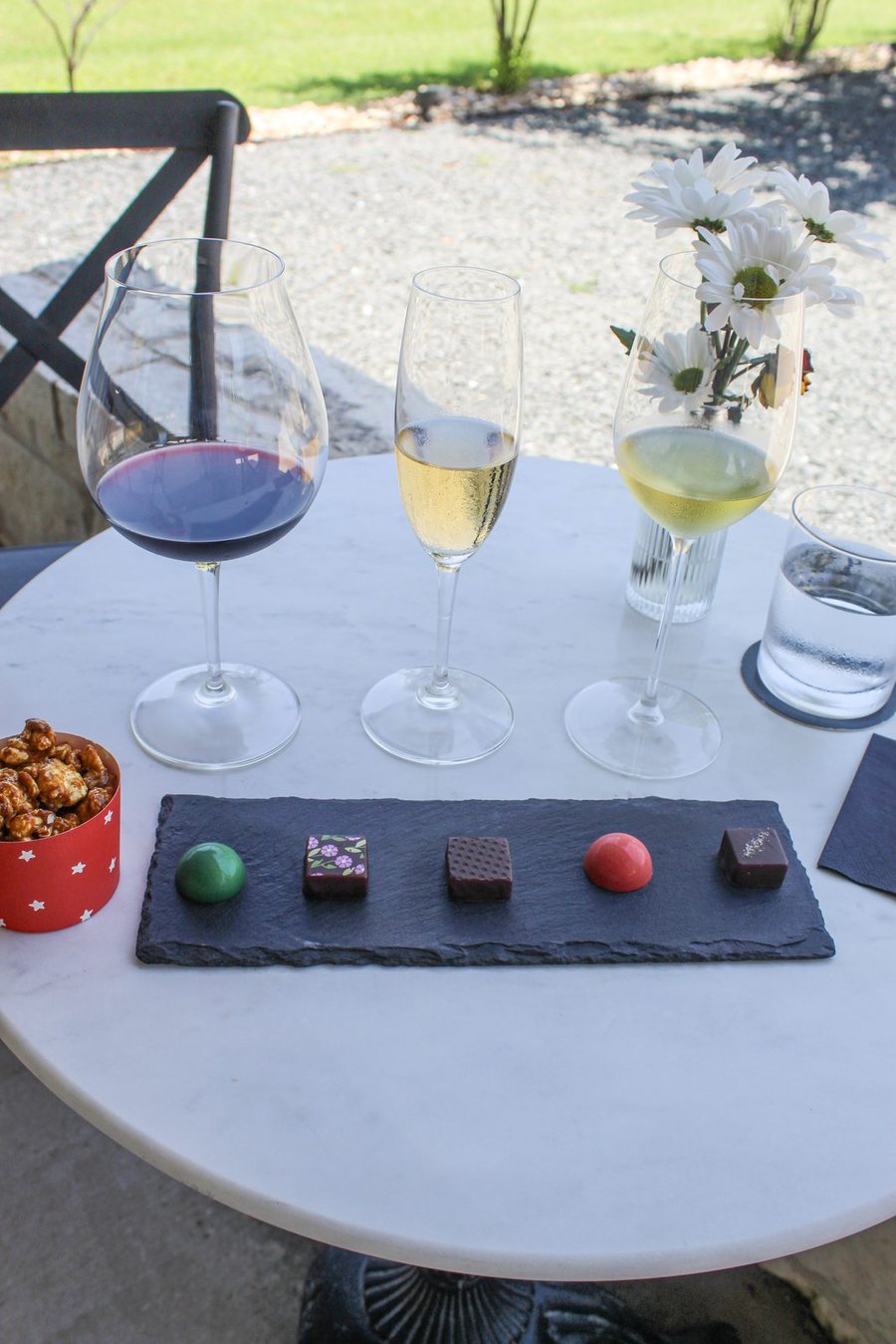 A red wine, a sparkling wine and a white wine beside a slate board of five bonbons and caramel popcorn