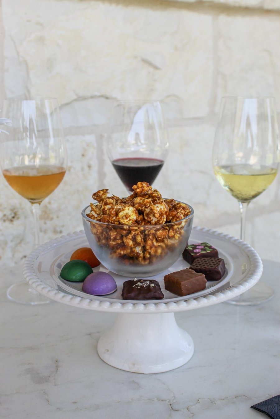 A cake stand holding a bowl of caramel popcorn ringed with colorful bonbons