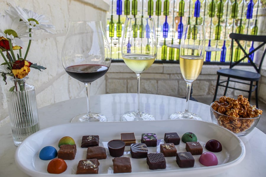 A long white platter of twenty assorted bonbons beside three glasses of wine and caramel popcorn