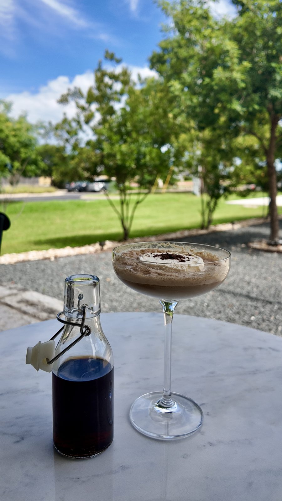 A Dr. Pepper coupe float topped with cream and shaved chocolate, beside a small glass bottle of syrup