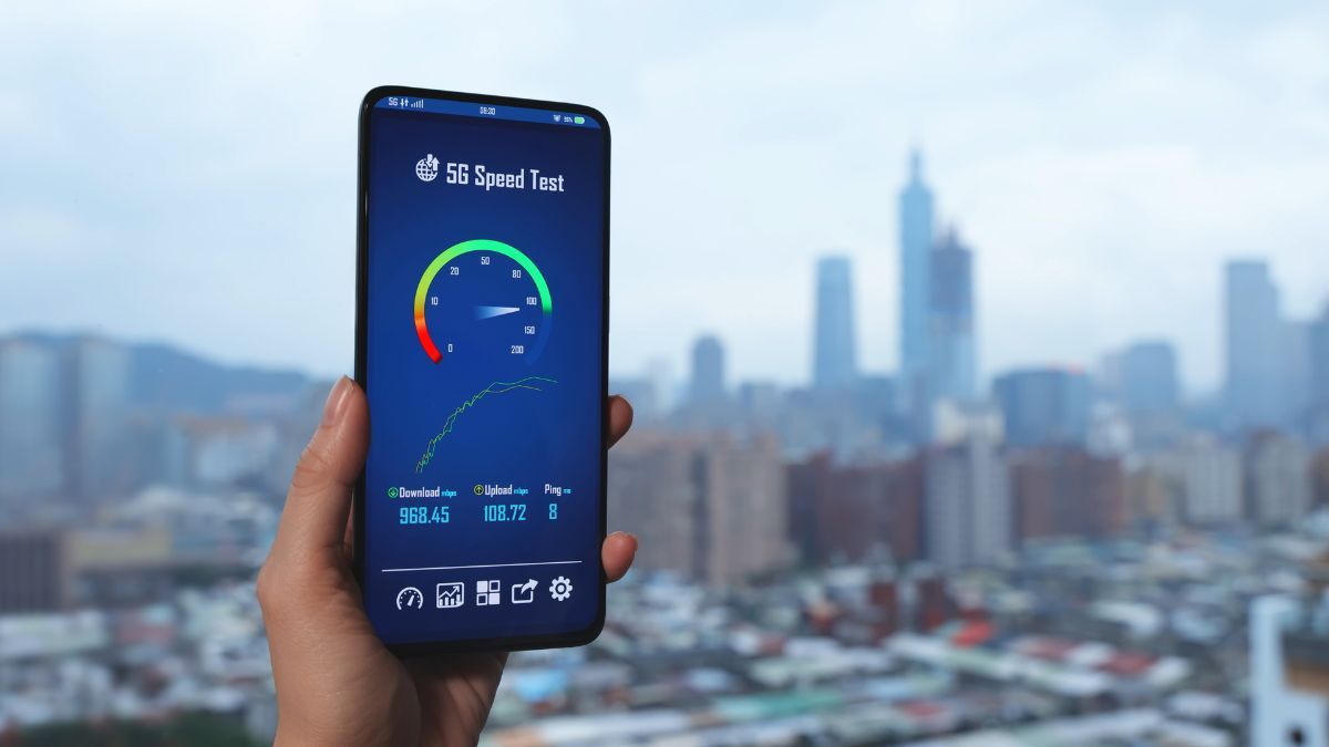 Hand holding a phone showing a 5G speed test with a city skyline in the background.