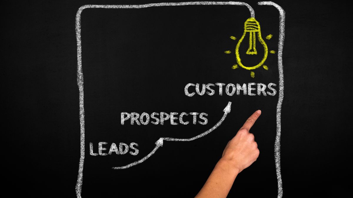 Hand pointing to a funnel on a chalkboard showing leads, prospects, and customers with a lightbulb at the top."