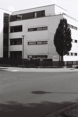 a tree next to a white mostly rectangular building with sign, WOHNUNGS GENOSSENSCHAFT DESSAU.