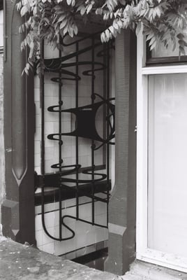a metal gate with a swirl design in front of a unevenly tile wall going downwards