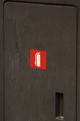 a white icon of a fire extinguisher in a matte red square on a black maintenance box with visible wear