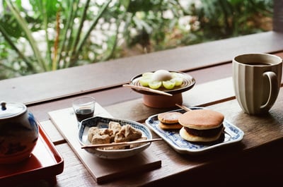 plates of dessert, tea, and coffee on a table by a window with greenery outside