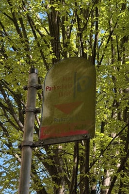 a parking sign on a pole in German heavily covered by moss in front of a tree
