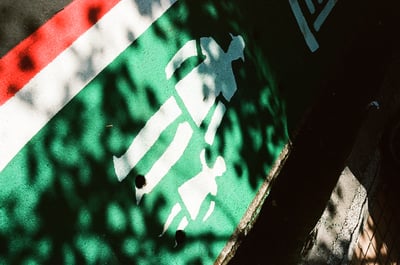 a green path and white sign of a person with hat holding a child painted on it. A pedestrian path.