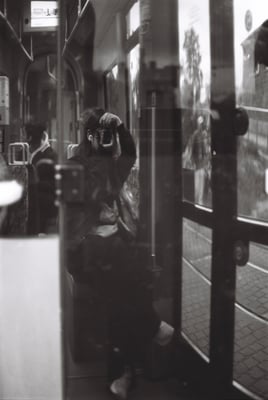 a woman wearing stripe sweater and sneakers taking a picture of themselves in the glass reflection on a tram