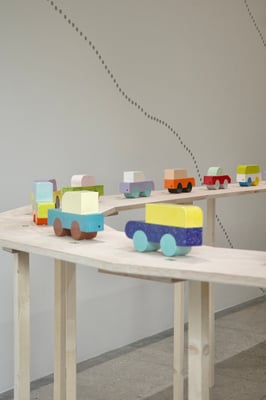 an array of colorful ceramic cars made of simple geometric shapes on a long display table