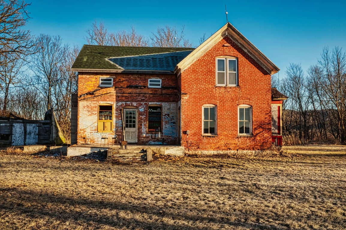 Original weathered two-storey brick house with a front-facing gable and bare trees.