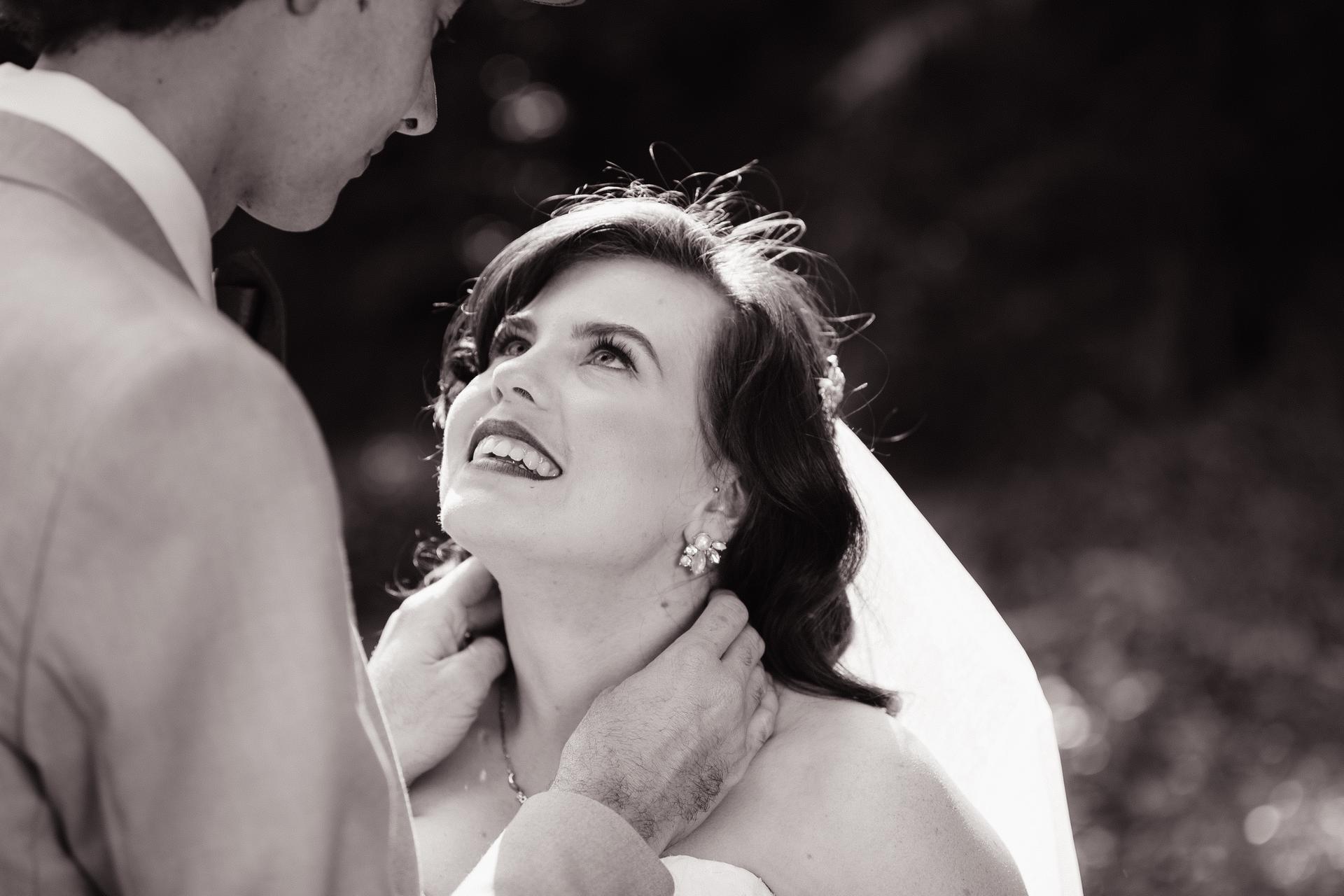 The bride Holly looks up at the groom Paul as he gently holds her neck outdoors at Kwila Lodge.