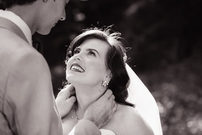 The bride Holly looks up at the groom Paul as he gently holds her neck outdoors at Kwila Lodge.