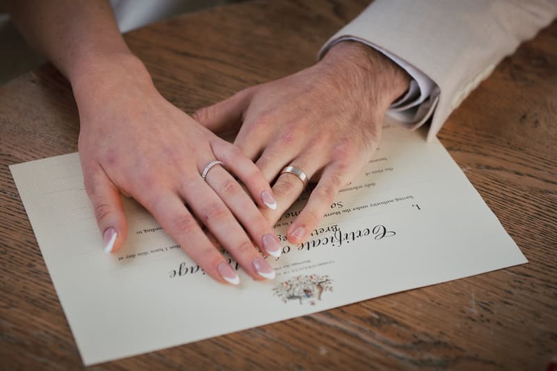 The bride and groom's hands rest on a wedding certificate at Sandstone Point Hotel — The Pavilion, showing their wedding rings.