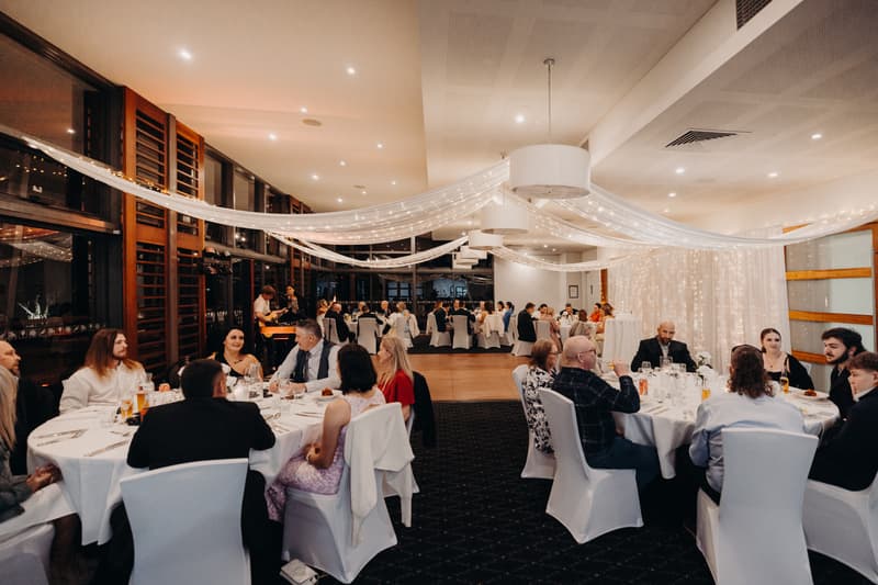 Guests are seated at round tables covered with white tablecloths in The Pandanus Room at The Tides during the wedding reception.