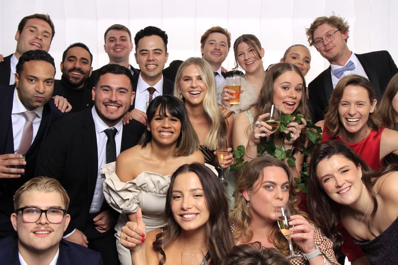 Group of guests posing joyfully in a photo booth with drinks and smiles.