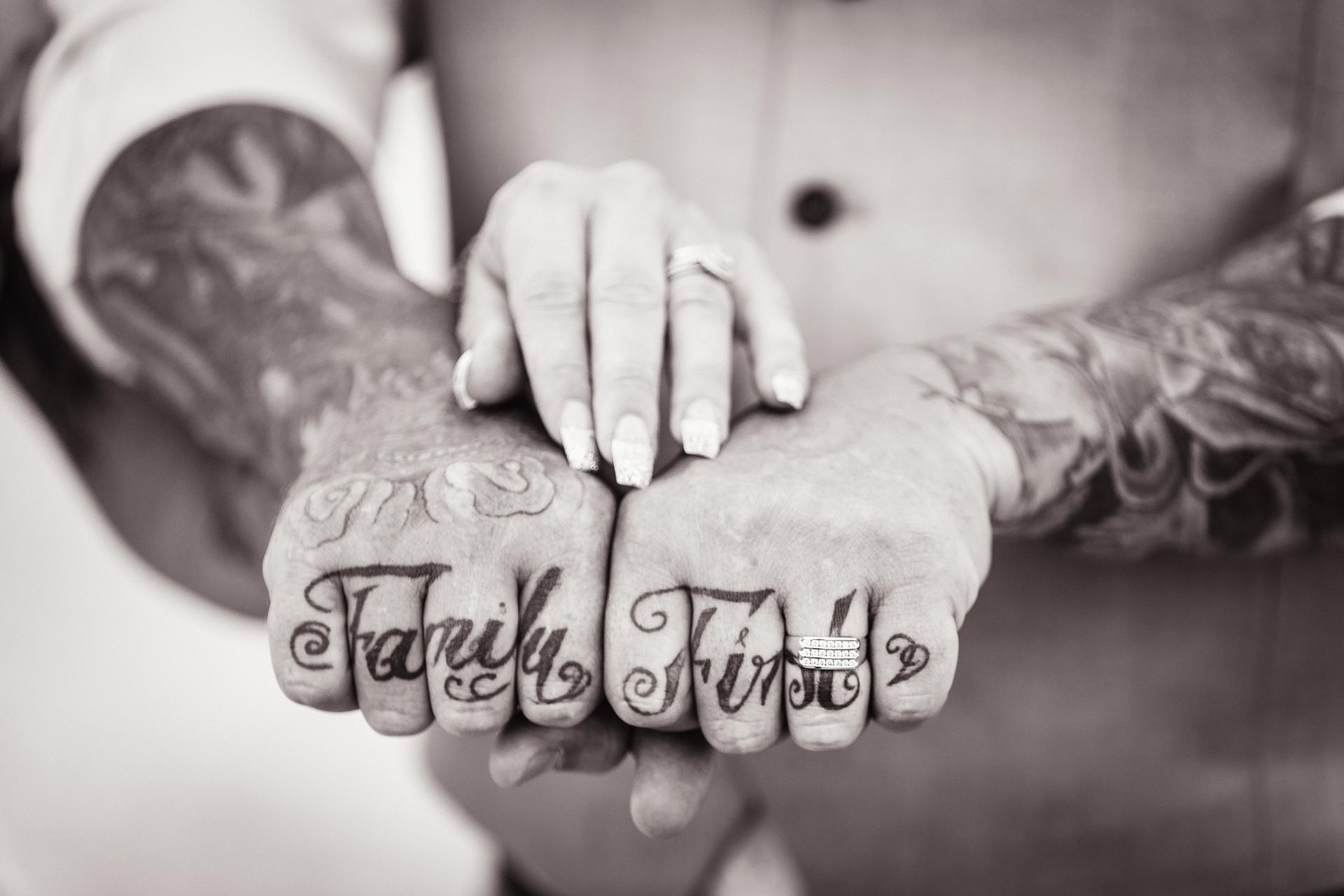 Close-up of the groom's tattooed fists with the words 'Family First' tattooed across the knuckles, and the bride's hand with a wedding ring resting on top.