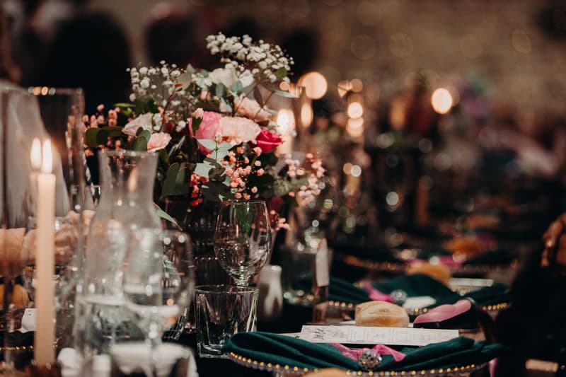 Close-up of a wedding reception table at Sandstone Point Hotel — Cellar, featuring floral centerpieces, candles, glassware, and place settings with menus and napkins.
