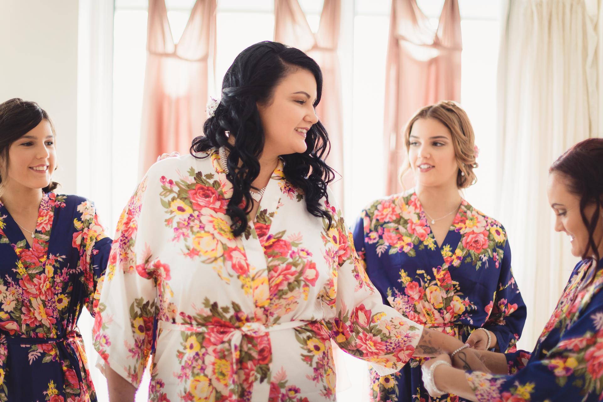 The bride Kelly wearing a white floral robe is surrounded by bridesmaids in matching blue floral robes at Novotel Sunshine Coast Resort during bridal preparation.