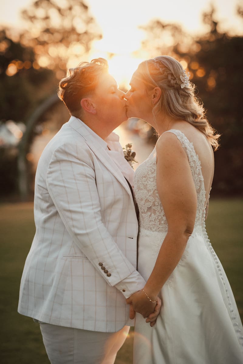 Brides Mandy and Selina share a kiss while holding hands outdoors. Gold Coast wedding videographer by She Said Yes.