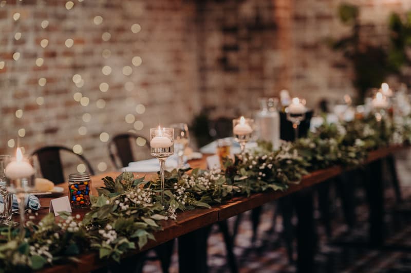 Long wooden table at Sandstone Point Hotel — Cellar decorated with greenery garland and floating candles in glass holders for the wedding reception.