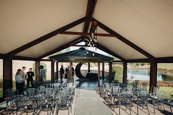 Empty ceremony seating area under a pavilion at Ocean View Estates — On The Lake with a crescent moon decoration on the altar and a few guests or staff standing near the back.