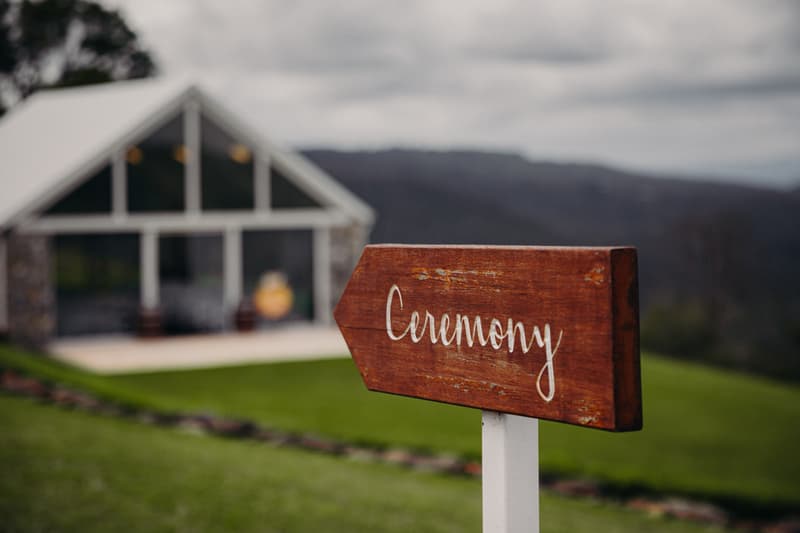 Wooden sign with 'Ceremony' written on it pointing towards a building at Preston Peak Winery Functions Centre.