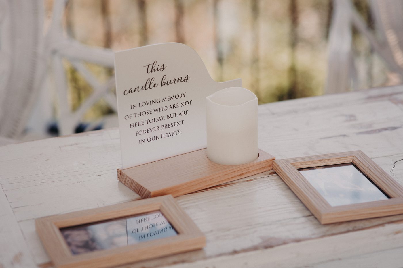A memorial candle and sign reading 'this candle burns in loving memory of those who are not here today, but are forever present in our hearts' displayed on a wooden table. Cinematic wedding photos by She Said Yes.