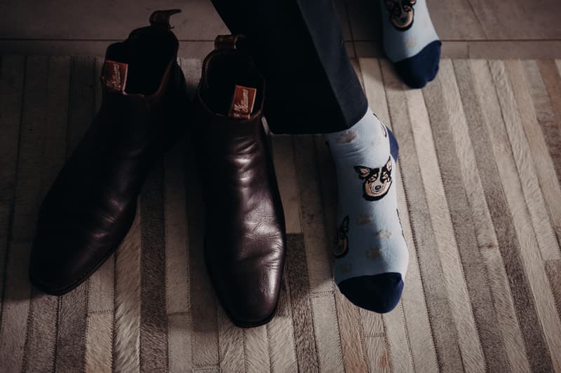 The groom's feet wearing light blue socks with dog faces and paw prints next to a pair of dark brown leather dress shoes on a striped rug at Preston Peak Winery Functions Centre.