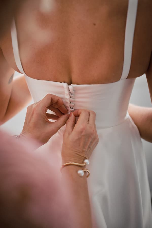 The mother of the bride fastens buttons on the back of the bride Ashleigh's wedding dress during bridal preparation.