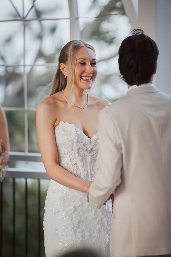 The bride Morgan and the groom Joel hold hands facing each other during their wedding ceremony at Sandstone Point Hotel — The Pavilion.