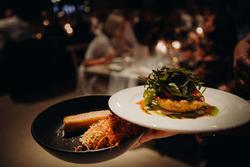 Two plates of food being served at the Preston Peak Winery Functions Centre reception, with guests and candlelight visible in the blurred background.