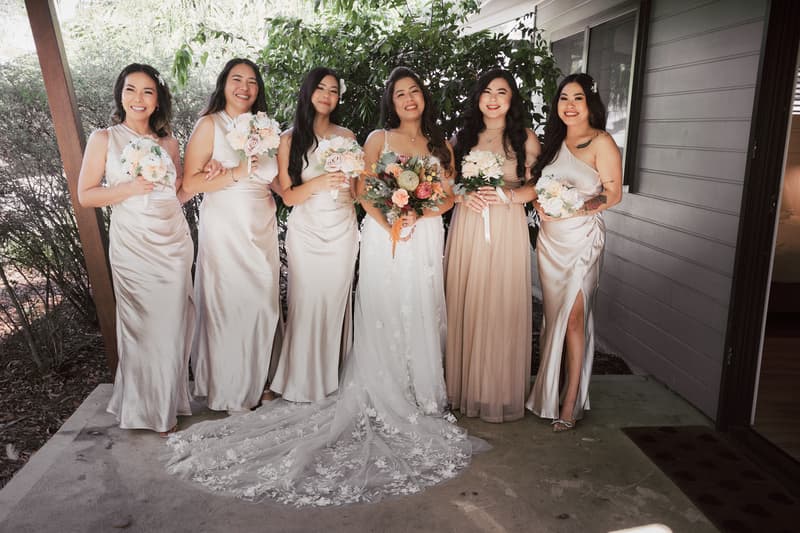 The bride Jheng stands with five bridesmaids holding bouquets outside near a building at Sandstone Point Hotel.