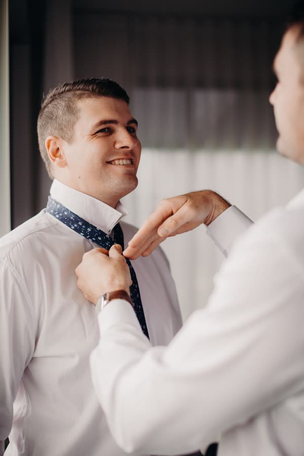 The groom Brent is having his tie adjusted by another man during preparation at Preston Peak Winery Functions Centre.