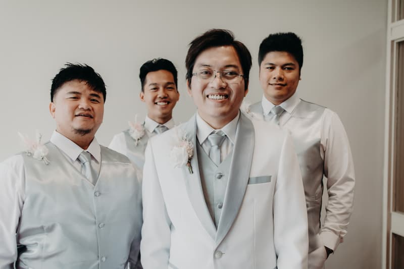 Timothy the groom stands with three groomsmen wearing matching silver vests and ties at Royal on the Park.