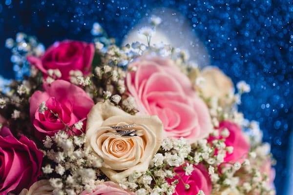 Close-up of a wedding bouquet featuring pink, cream, and white roses with baby's breath flowers, with two wedding rings placed inside a cream rose at Bilinga Beach Weddings — Bilinga SLSC.