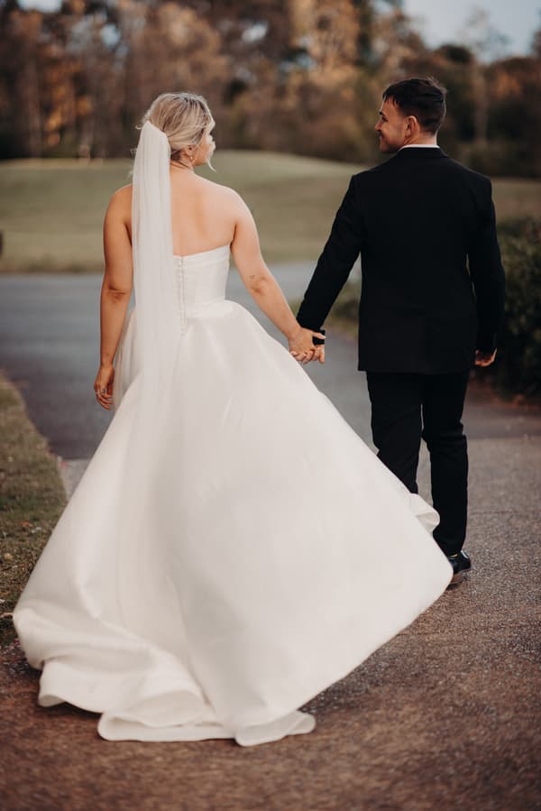 Bride Libby and groom Kyle walk hand in hand outdoors at The Tides during their couple portraits session.