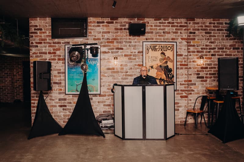 A man stands behind a DJ booth with microphone and sound equipment against a brick wall at Sandstone Point Hotel — Cellar.