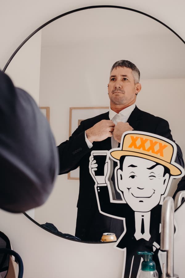 The groom Kyle adjusts his tie while looking into a round mirror at The Tides.