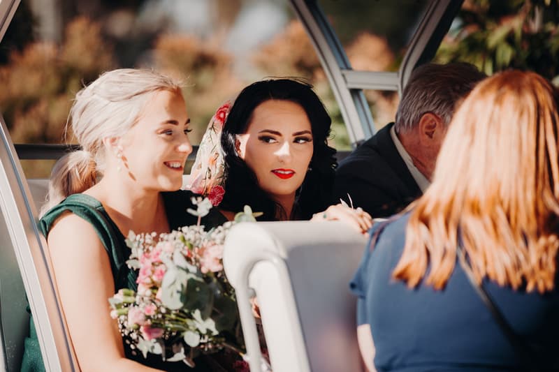 The bride Mindy and a bridesmaid sit together holding a bouquet, with two other guests partially visible, at Sandstone Point Hotel — Pavilion.