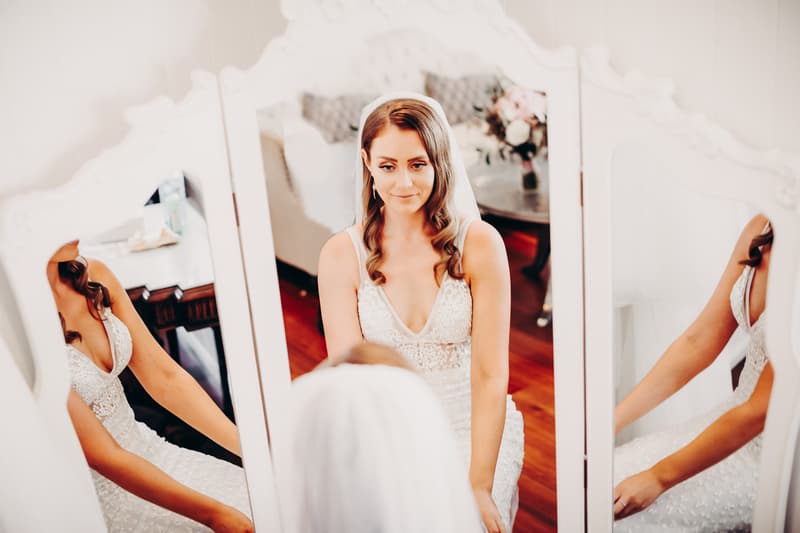The bride Chelsea sits in front of a three-panel mirror wearing her wedding dress and veil at Preston Peak Winery Functions Centre.