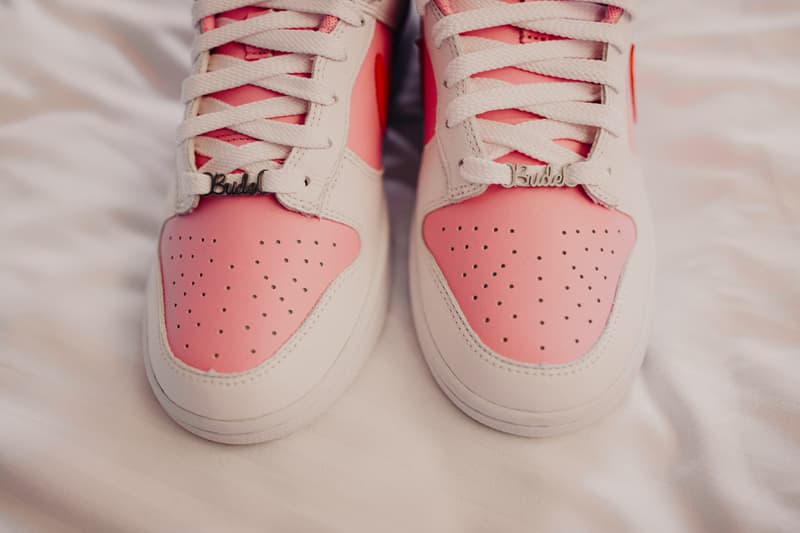 Close-up of pink and white sneakers with 'Bride' charms on the laces placed on a white fabric surface.