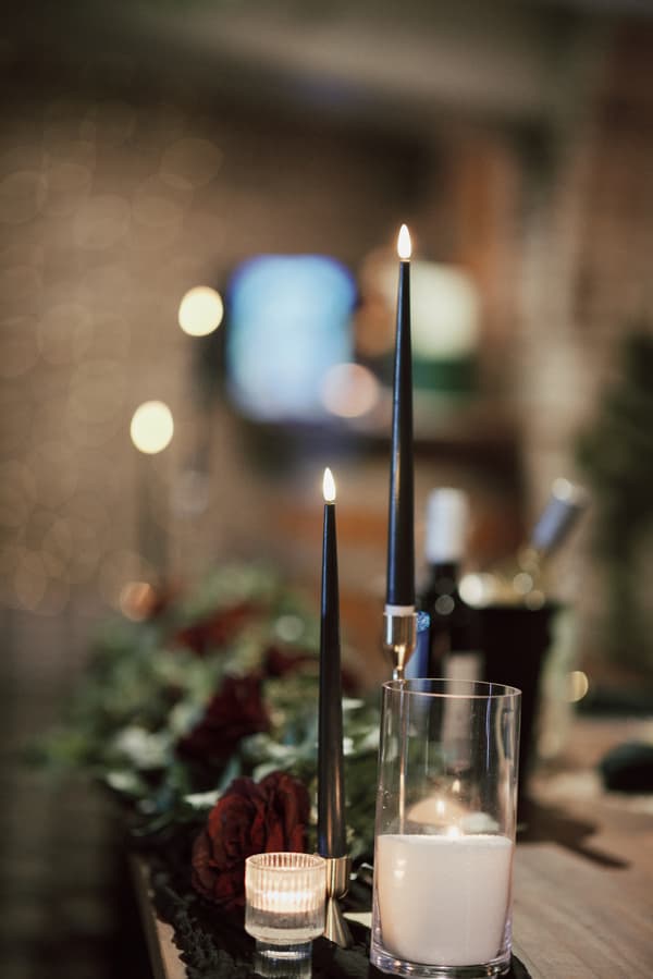 Close-up of lit black taper candles and a white pillar candle in a glass holder on a decorated table at Sandstone Point Hotel — The Cellar.