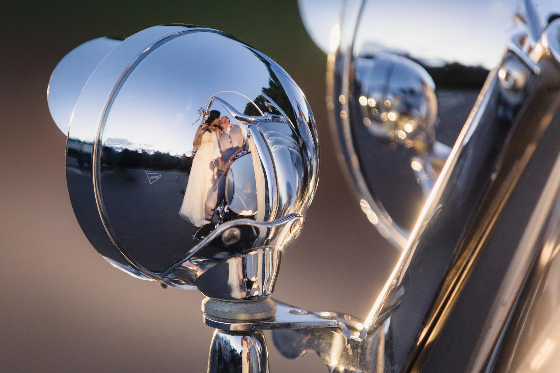 The bride Kelly and groom Shane are reflected kissing in the chrome headlight of a vintage car at Novotel Sunshine Coast Resort during their wedding day.