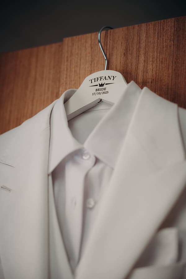 White suit jacket and shirt hanging on a personalized hanger labeled 'Tiffany Bride 17/10/2025'.