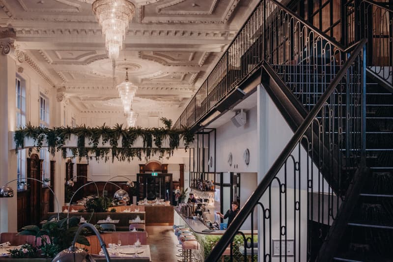 Interior of Donna Chang showing the reception area with tables set for guests, a bar with staff behind it, decorative hanging greenery, and ornate ceiling chandeliers.